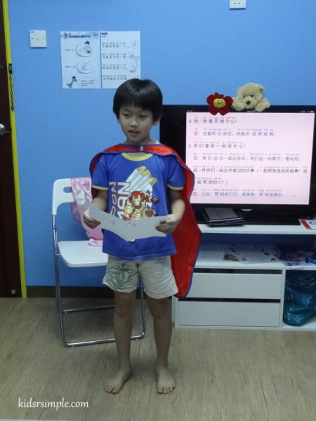 My boy wearing a cape and reading to the class.